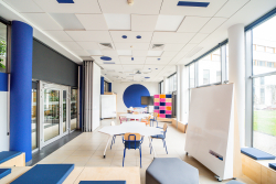 Duża, otwarta sala z białą tablicą i niebieskimi krzesłami, idealna do spotkań i współpracy.