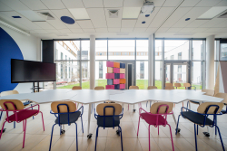 Przestronny pokój z krzesłami i stołami, z dużym oknem, stworzony do wspólnej pracy i kreatywnych spotkań.