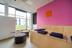 Przytulny pokój w odcieniach różu i pomarańczy, z ławką i oknem, sprzyjający współpracy i kreatywności.