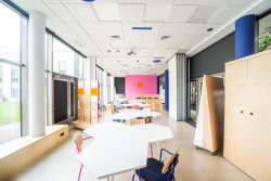 Klasa z kolorowymi meblami i stołami, stwarzająca radosną atmosferę do nauki i kreatywności.