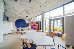 Klasa z rzędem stołów i krzeseł, gotowa na zajęcia i naukę w przyjaznej atmosferze.