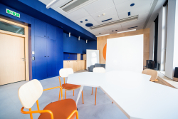 Biuro w odcieniach niebieskiego i pomarańczowego z białymi stołami i krzesłami, tworzące nowoczesną przestrzeń pracy.