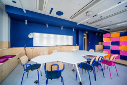 Wnętrze klasy z różnokolorowymi krzesłami i stołami, zachęcające do kreatywności i współpracy