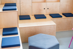 Przestrzeń z drewnianymi ławkami, niebieskimi poduszkami i pufą, idealna do kreatywnej współpracy.