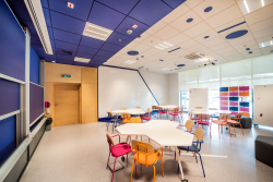 Wnętrze klasy z różnokolorowymi krzesłami i stołami, sprzyjające interakcji, kreatywności i zaangażowaniu.