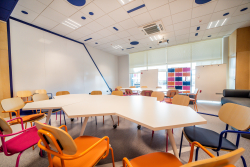 Wnętrze klasy z różnokolorowymi krzesłami i stołami, sprzyjające kreatywności i interakcji.